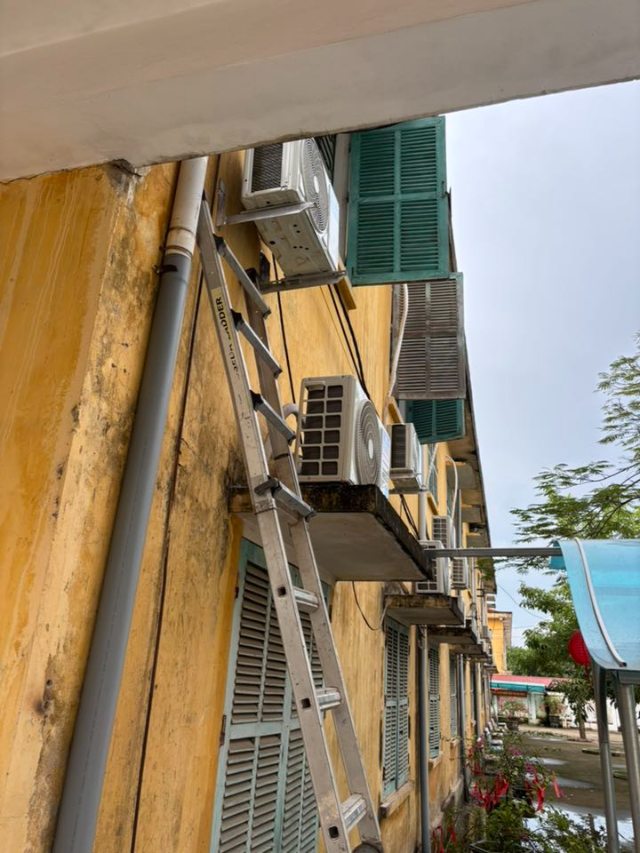 Nhiều dàn nóng được lắp thẳng hàng ngoài hành lang, có giá đỡ chắc chắn, kỹ thuật viên dùng thang tiếp cận